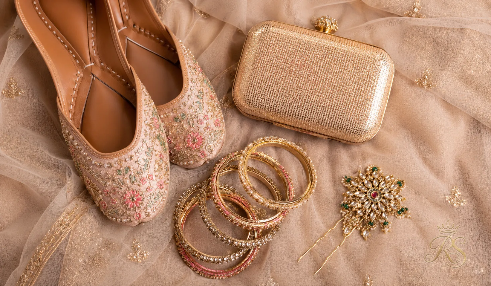 Flatlay of bridal accessories: embroidered juttis, a metallic clutch, bangles and a jadau hairpin