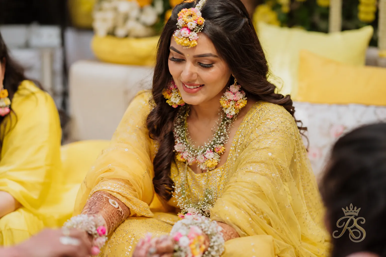 Bride at a mehndi ceremony wearing fresh floral jewellery and a yellow outfit