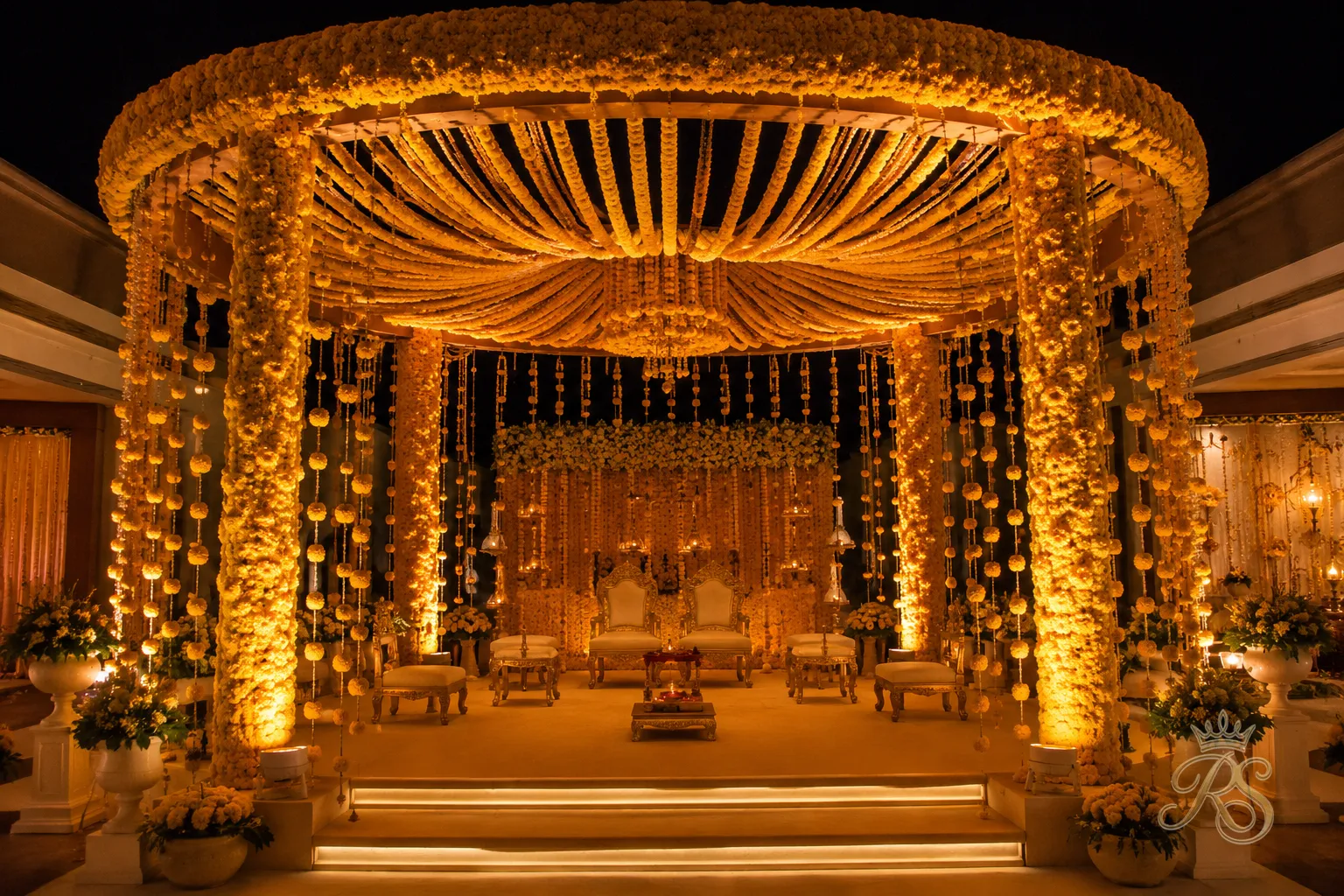 Wedding mandap decorated with a monochrome marigold floral installation and warm lighting