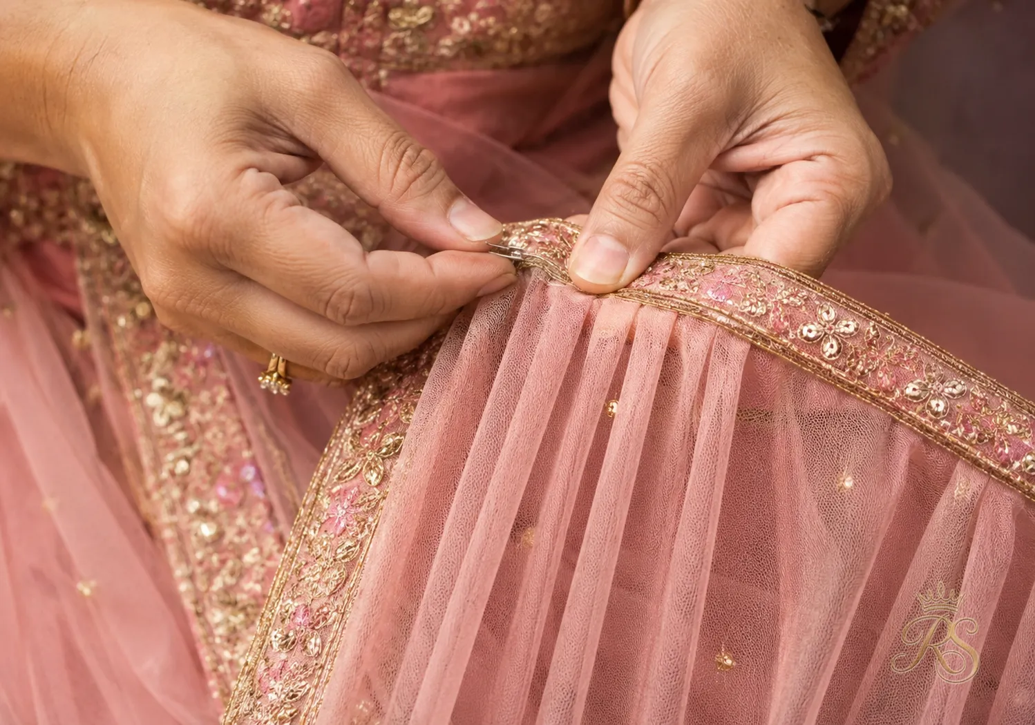 Hands demonstrating how to pin pleats into a bridal dupatta using safety pins