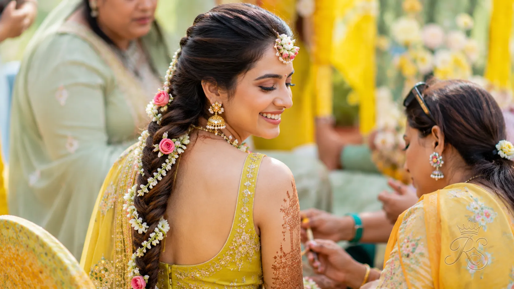 Bride at mehendi ceremony with a large floral braid woven with jasmine and roses