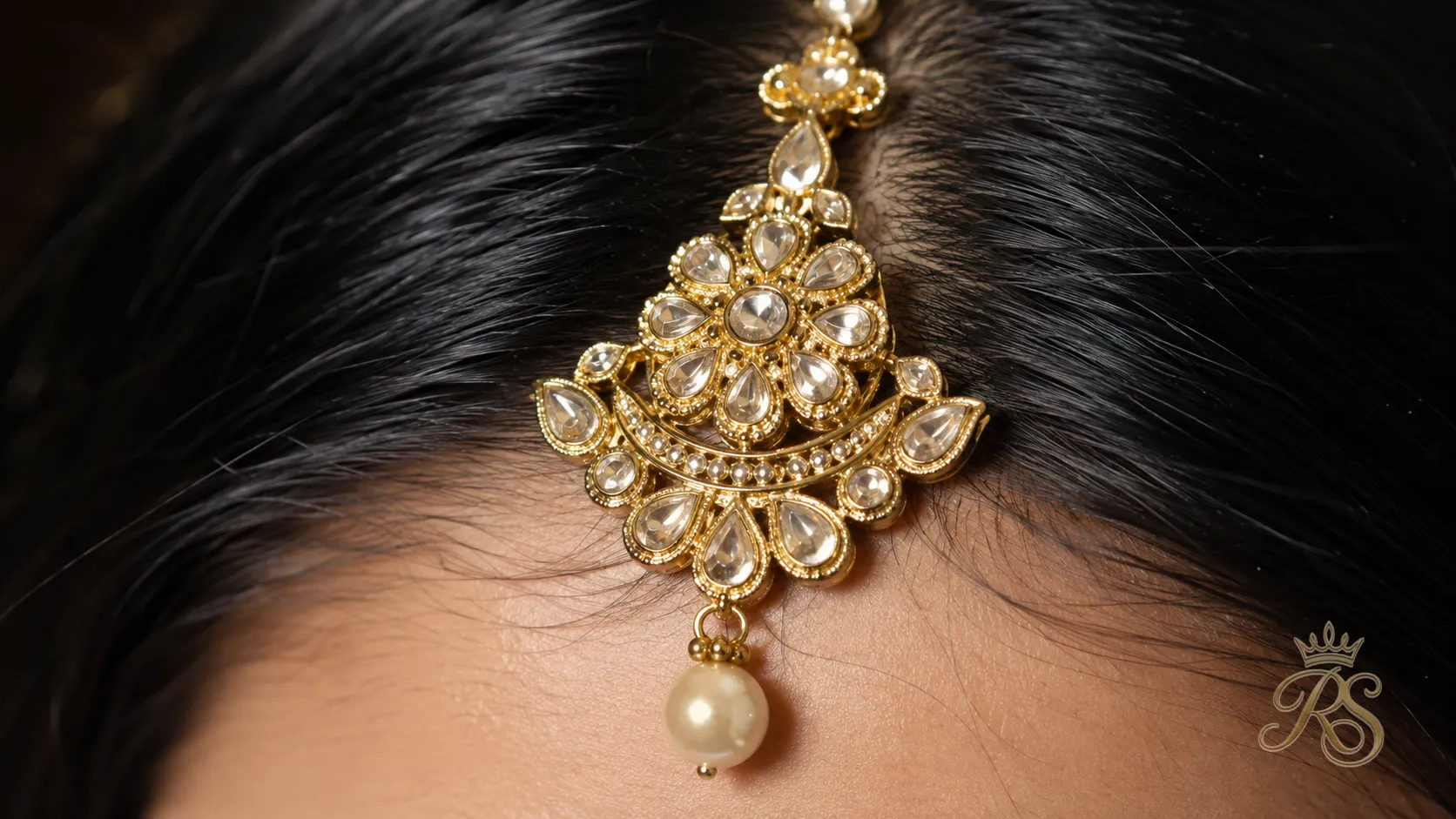 Close-up of an ornate bridal maang tikka with hanging pearl drop