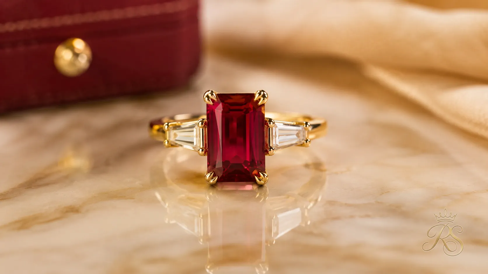 Emerald cut ruby engagement ring set in yellow gold on a marble surface