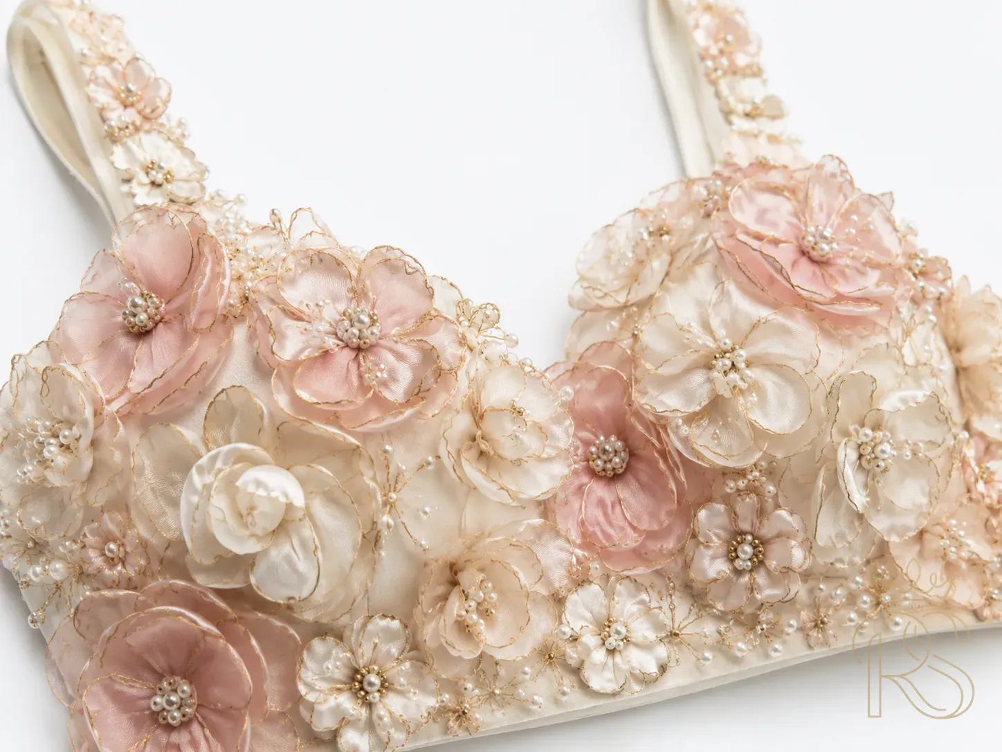 Close-up of Indian bridal blouse covered in hand-crafted 3D fabric flowers in ivory and pale pink, intricate petals with gold-tipped edges, some flowers with pearl centres, editorial fashion close-up photography, white background