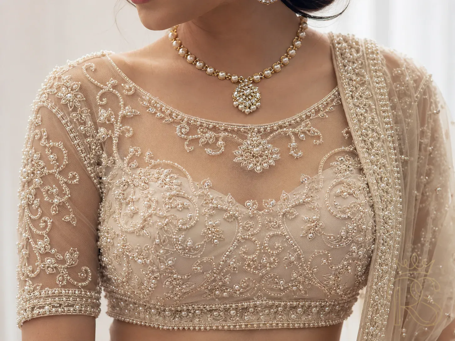 Close-up of an Indian bride's sheer net blouse with intricate pearl and threadwork embroidery creating an illusion effect on the neckline and sleeves, close-up fashion photography, soft white studio lighting