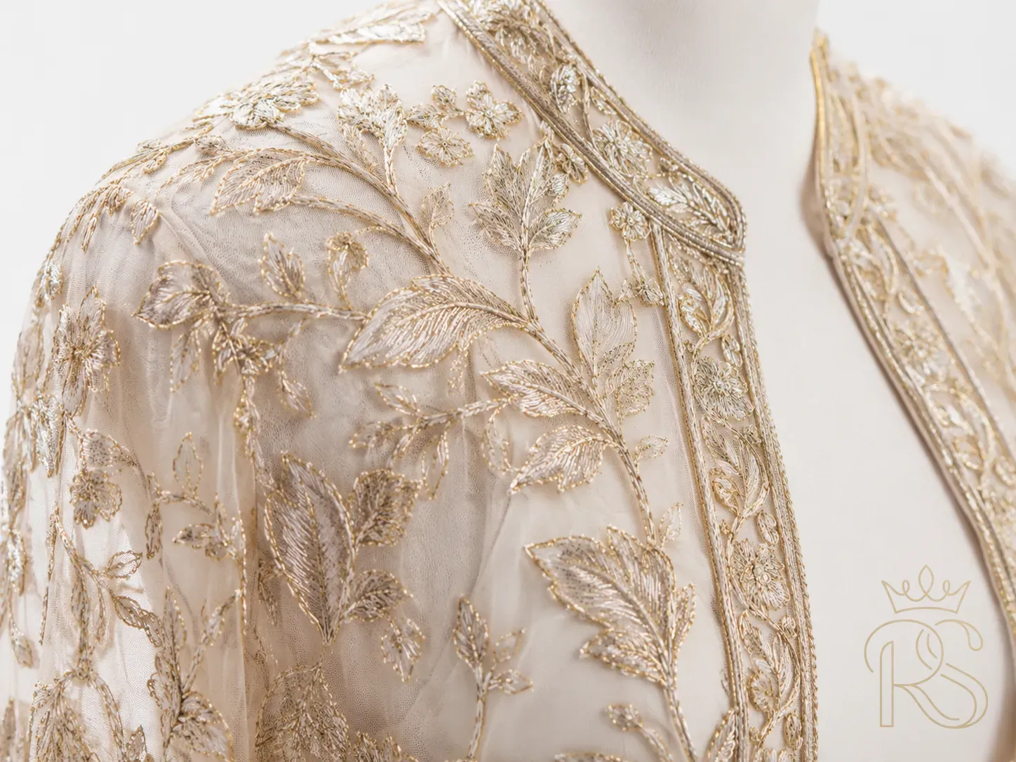 Close-up of delicate sheer embroidered bridal jacket detail, fine gold thread embroidery on transparent net fabric, macro fashion photography, white background
