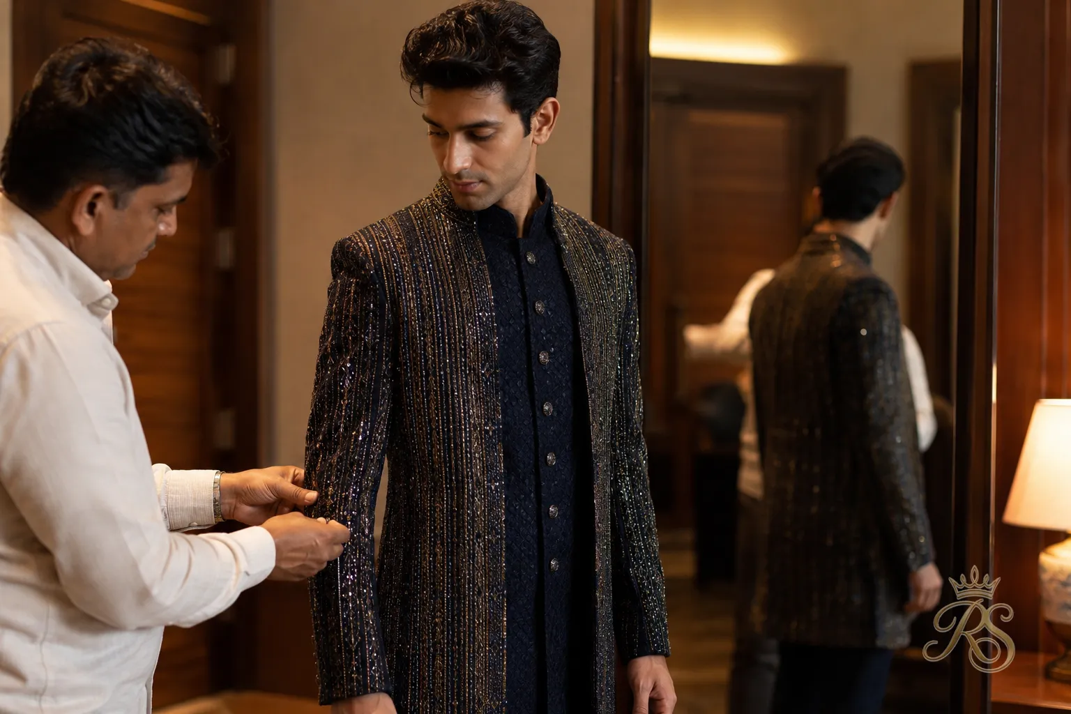 Slim-built groom trying on a sangeet outfit with a tailor adjusting the fit