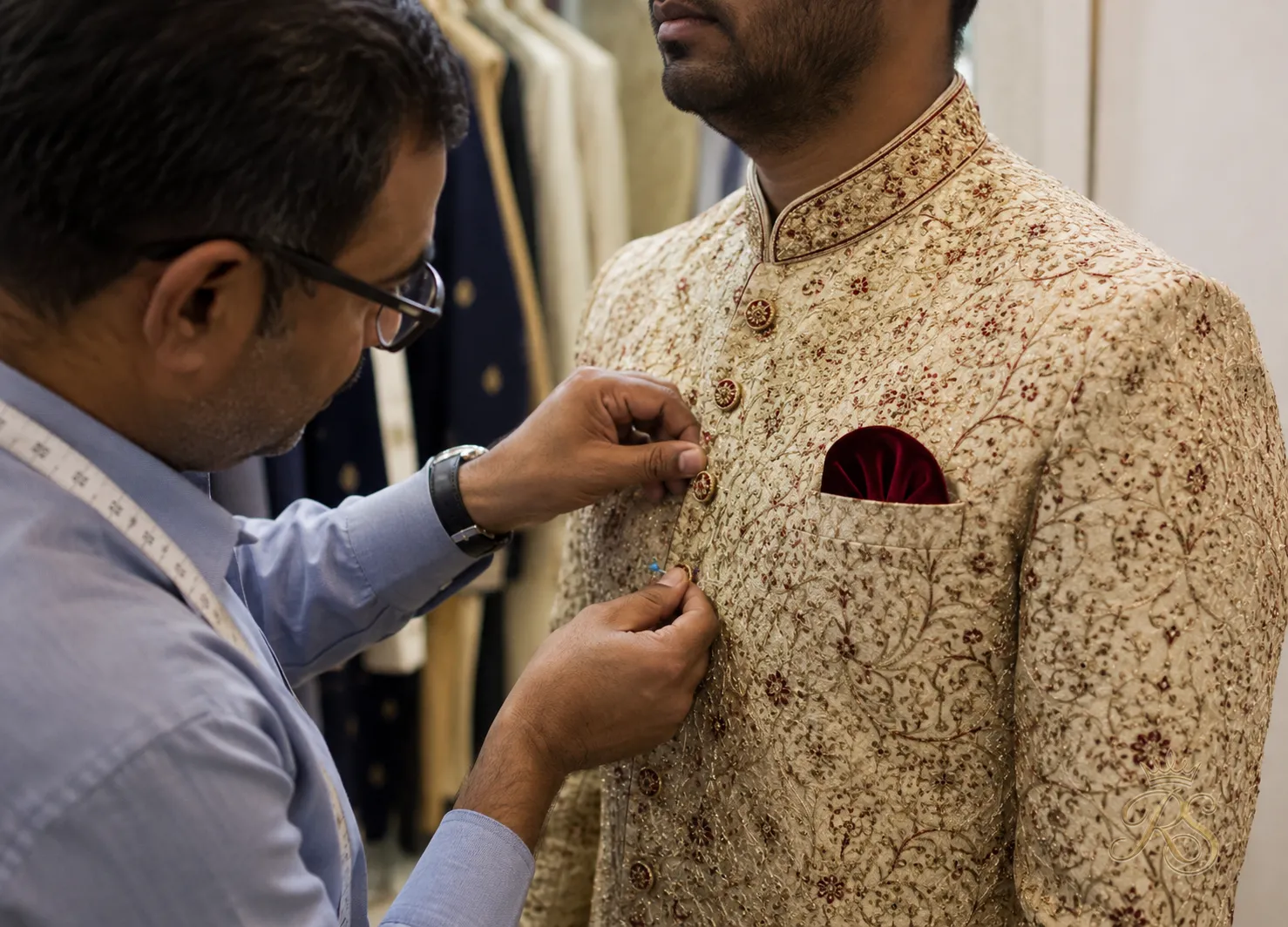 Tailor pinning and adjusting a groom's sherwani during a fitting session