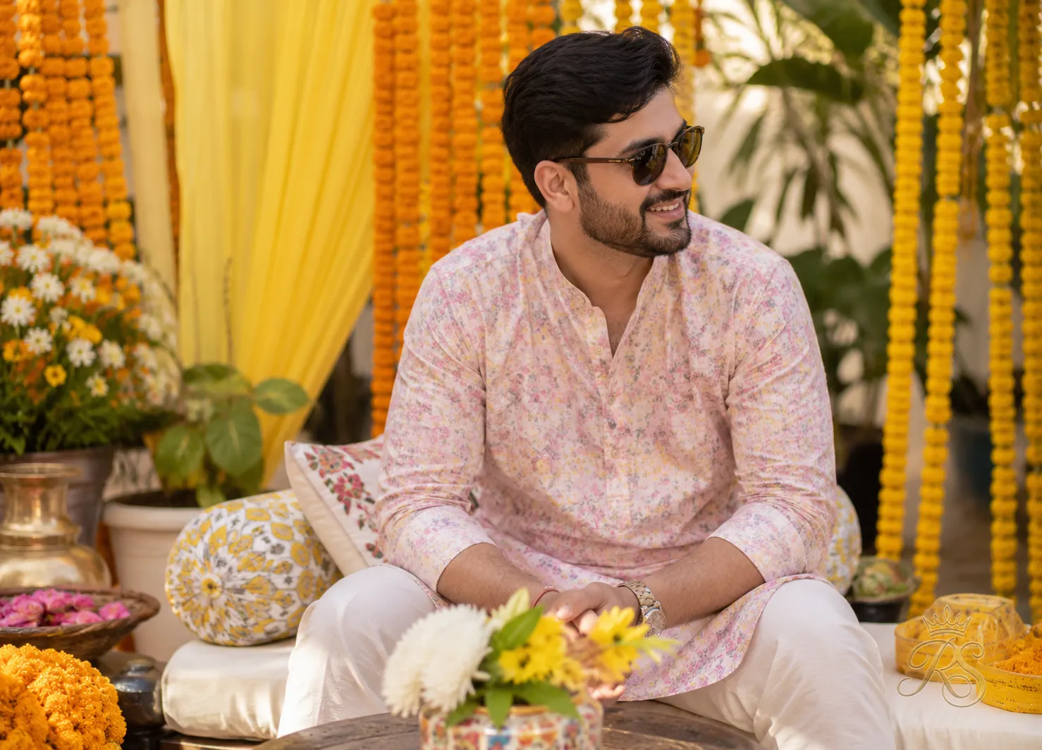 Groom in a pastel printed kurta for the mehndi ceremony surrounded by flowers
