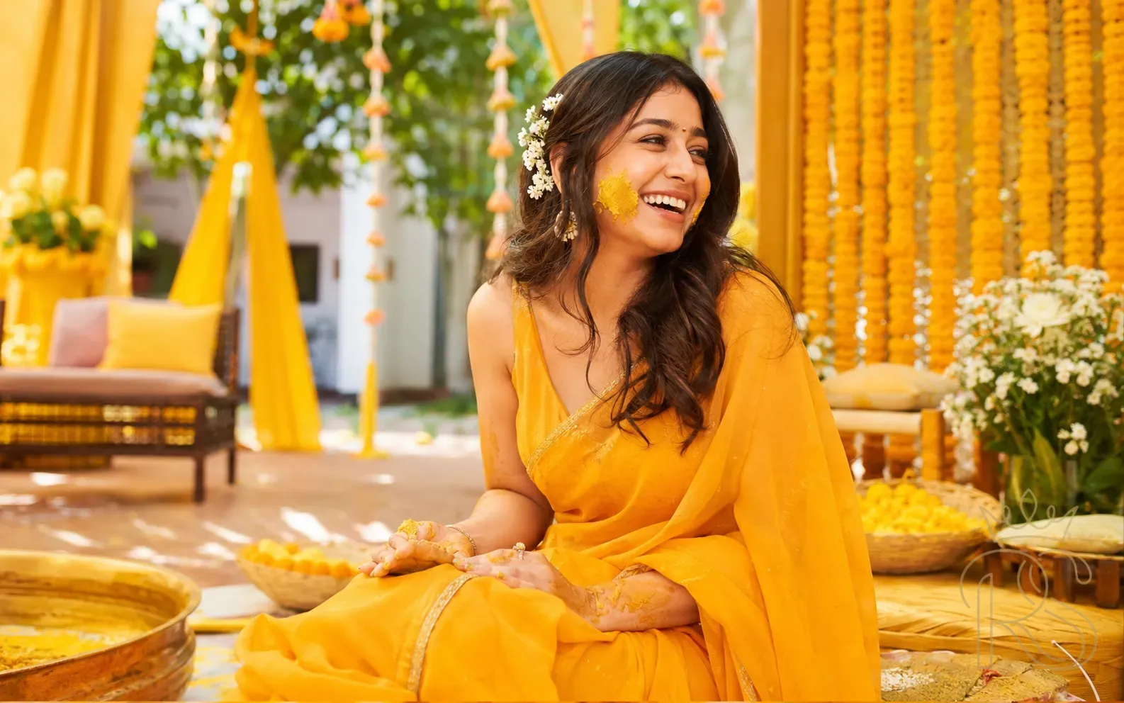 Indian woman in marigold orange saree with jasmine flowers in hair laughing at Haldi ceremony