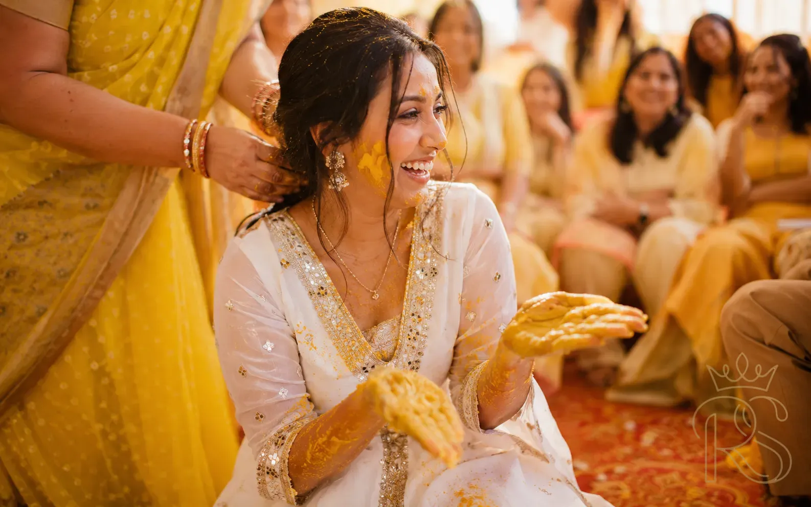Indian woman in white anarkali with gold border and turmeric stains on hands at Haldi ceremony
