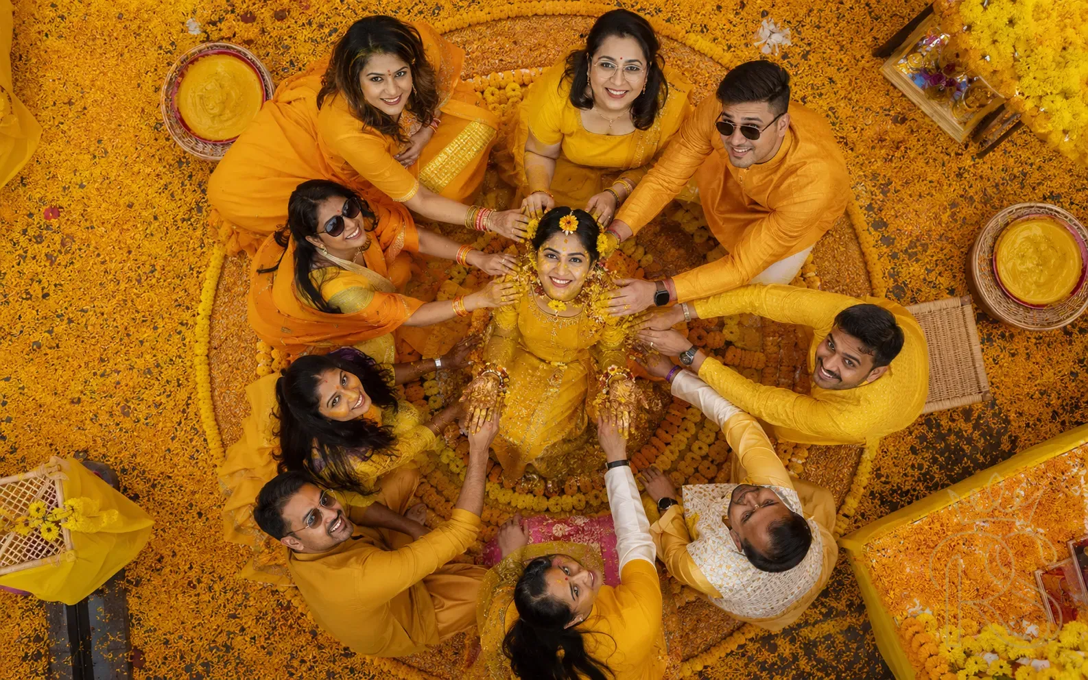 Bird's eye drone view of Indian Haldi ceremony with bride in yellow centre surrounded by family in yellow and orange