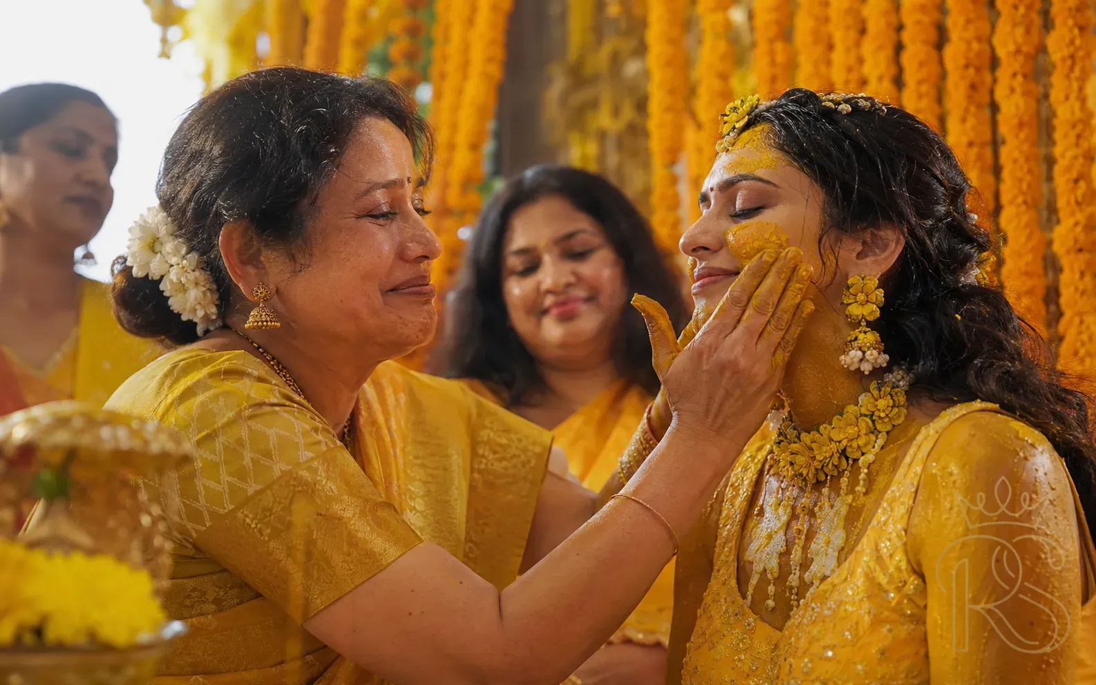 Candid intimate moment of Indian mother applying haldi to bride's face with emotional expression in morning light