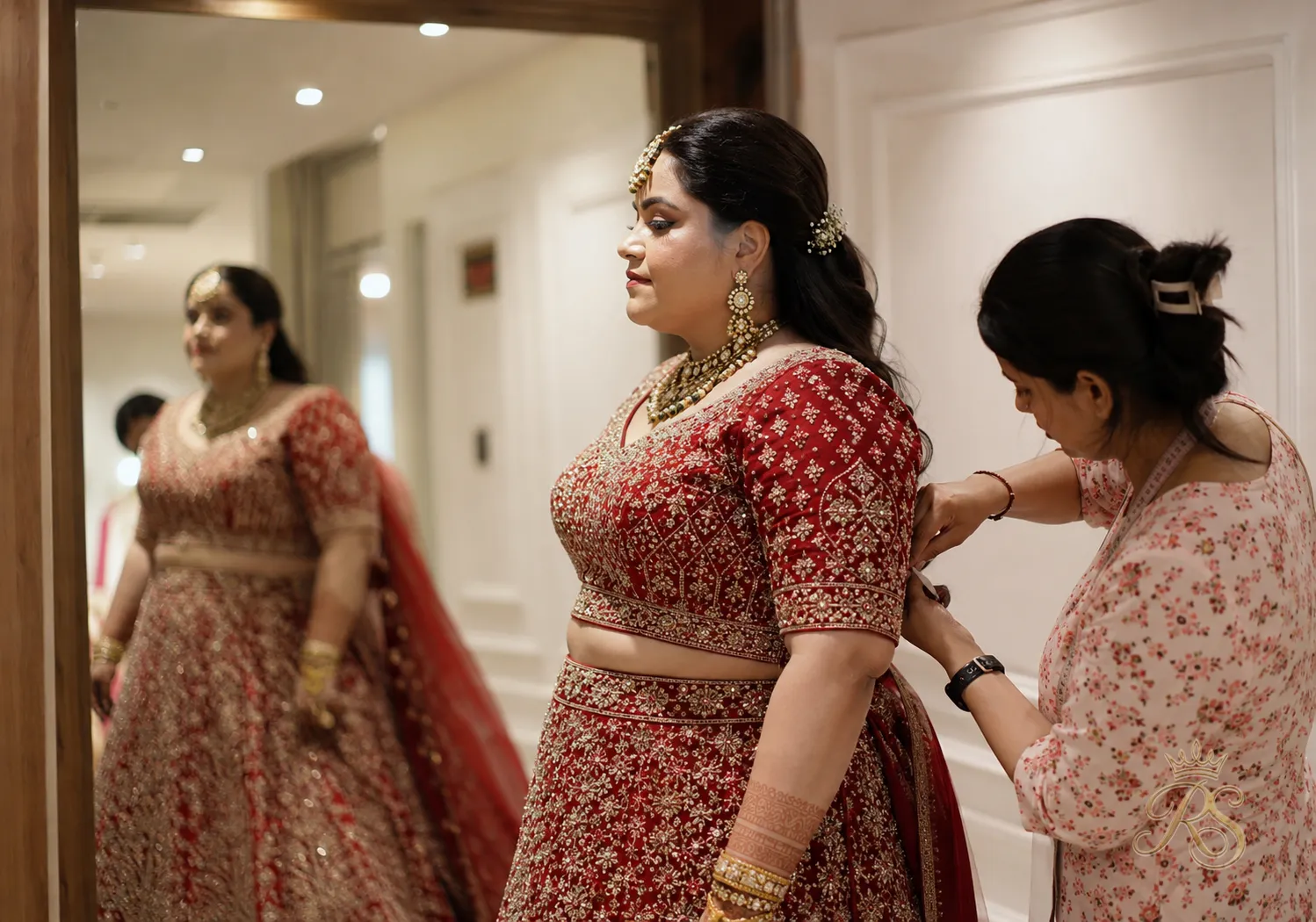 Bride during a final trial fitting for her bridal lehenga with a tailor pinning adjustments