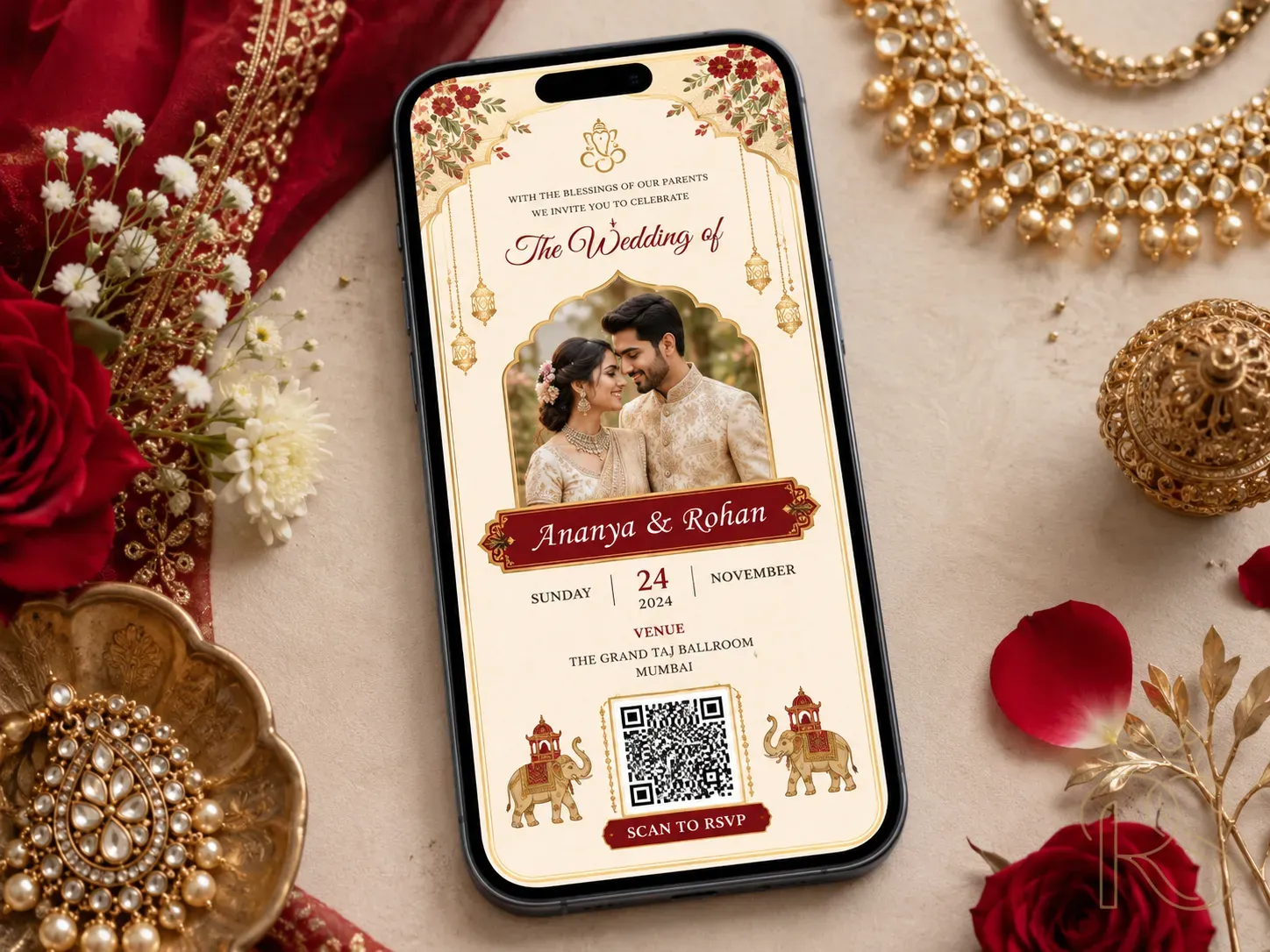 Beautiful Indian digital wedding invitation design displayed on a smartphone screen — elegant gold and red design with traditional motifs, couple's photo, QR code for RSVP, shown in a lifestyle flatlay with flowers and jewellery around the phone, top-down photography