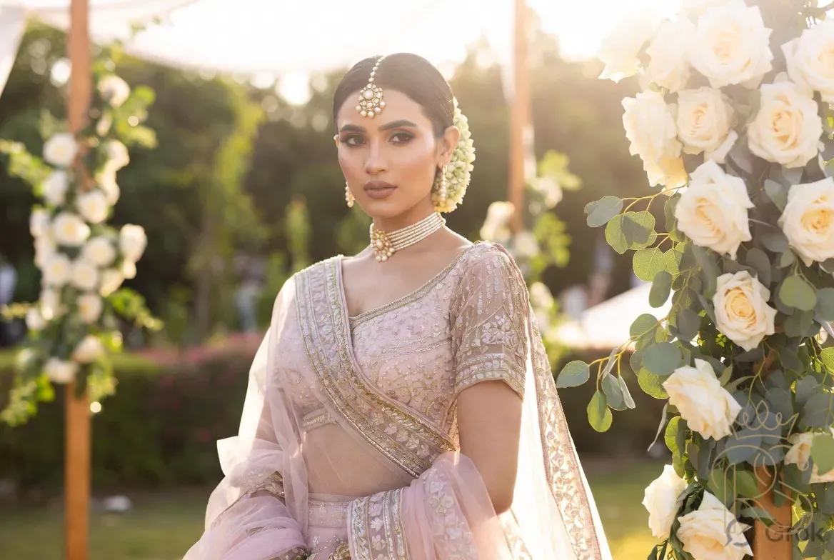 Indian bride in pastel pink lehenga standing in a garden mandap with pastel floral décor