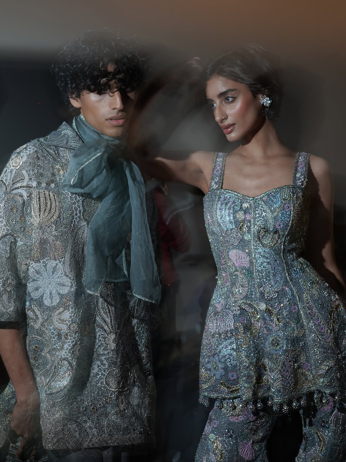 Two models backstage for Aisha Rao in heavily beaded silver garments with a teal organza scarf