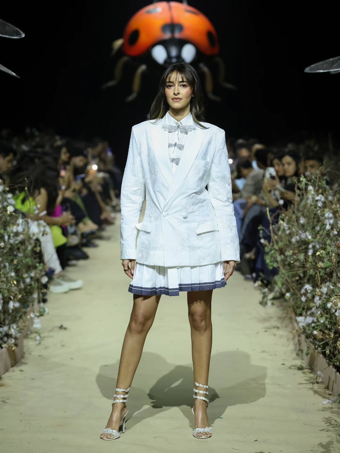 Ananya Panday walks the finale runway for SUPIMA presents AFEW by Rahul Mishra in a white embroidered blazer and pleated skirt, with a giant ladybug installation overhead