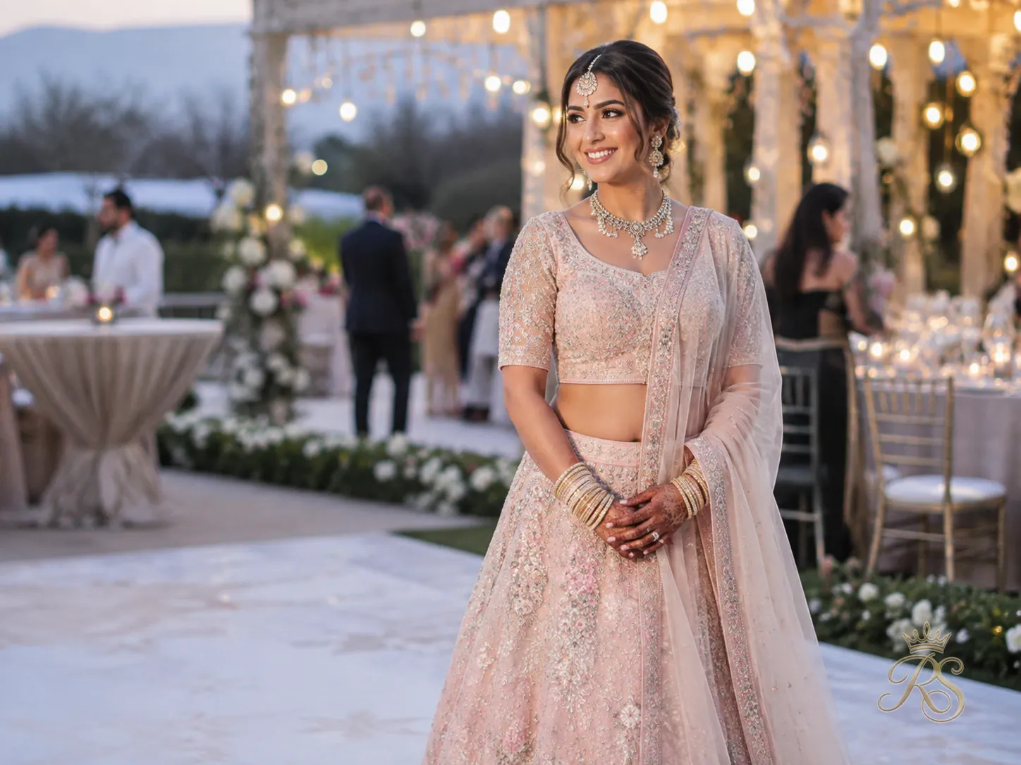 Bride in a pastel-toned bridal lehenga standing in soft evening light at an outdoor wedding venue