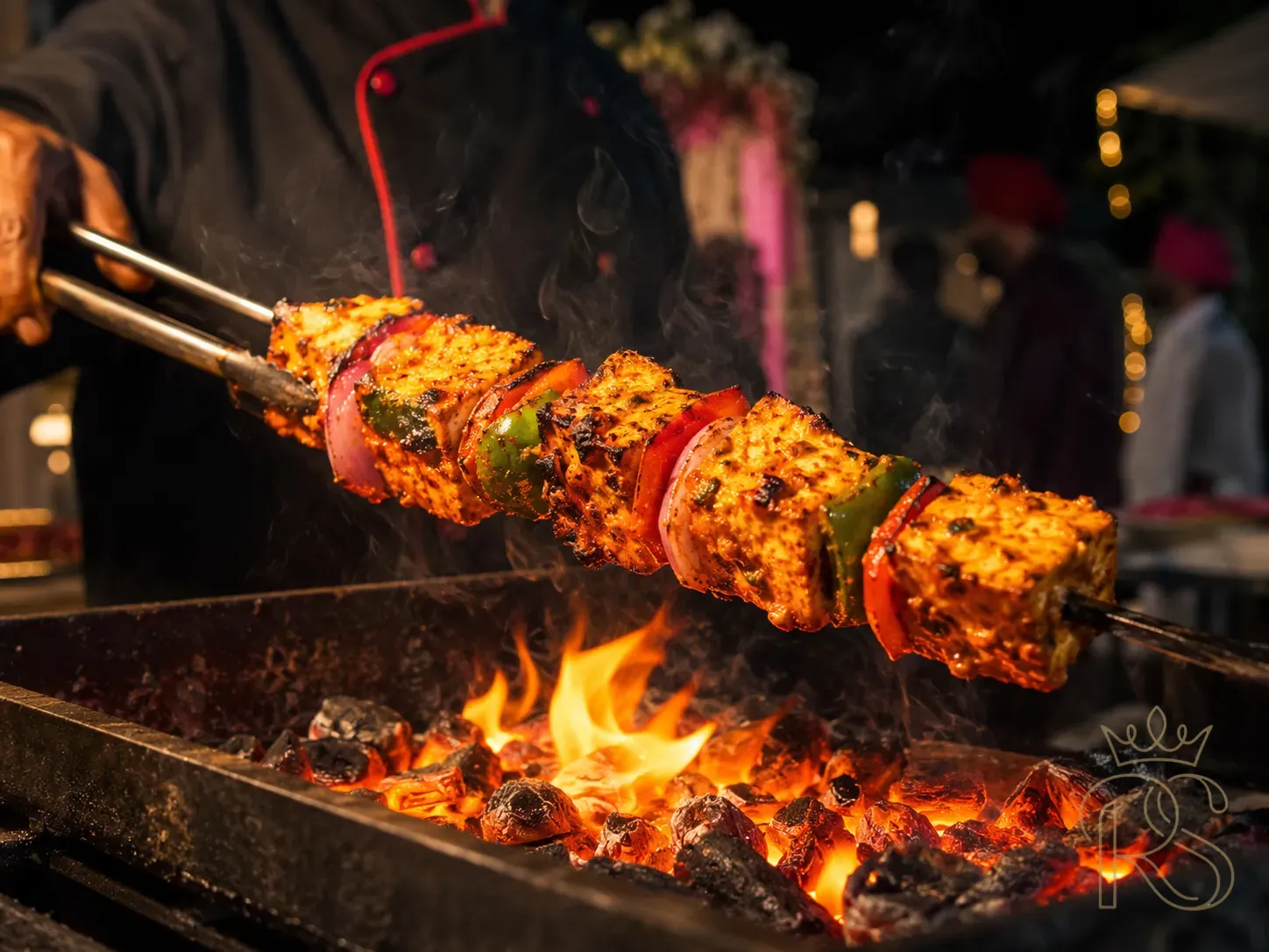 Paneer tikka on iron skewer at Indian wedding live grill — thick cubes of marinated paneer with charred edges, bell peppers and onion between pieces, chef's tong holding the skewer above glowing orange coals, flames visible underneath, steam rising, food photography, warm firelight, moody dark background, action shot