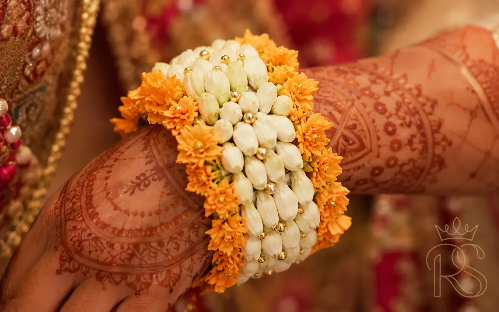Indian bride's wrist with fresh flower wrist cuff of tuberose and marigold over fresh mehndi henna in warm light