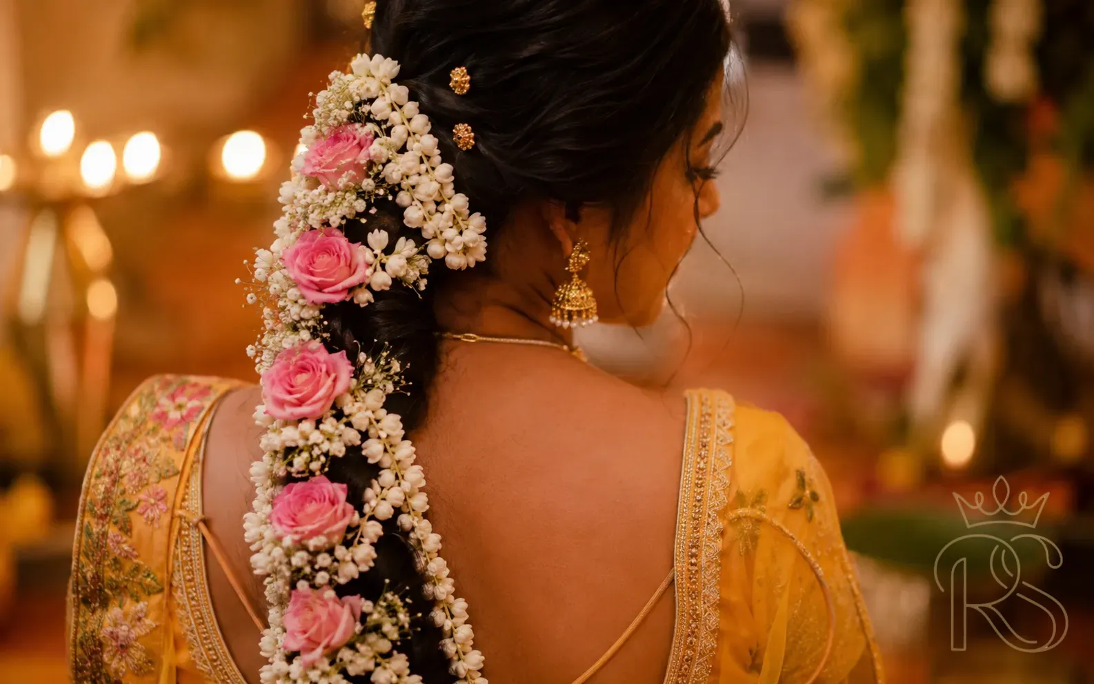 Indian bride with intricate jasmine and rose flower veni woven through dark braid with gold pins at Mehendi ceremony