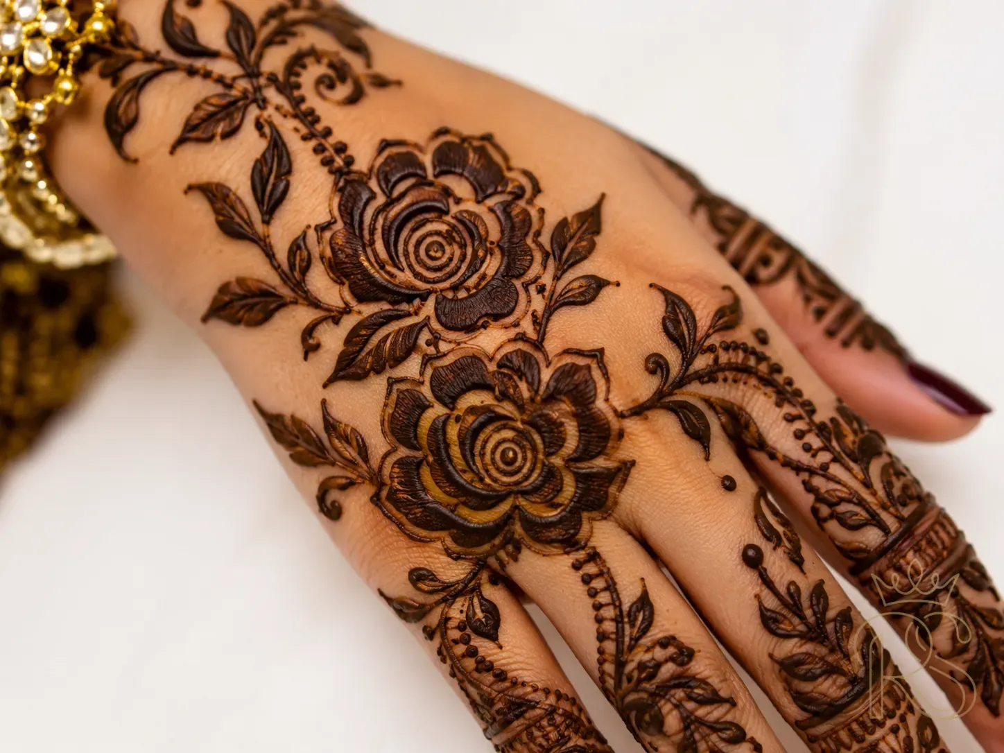 Bold Arabic mehndi with large open floral motifs, thick lines and trailing vines on bride's hand in deep brown henna