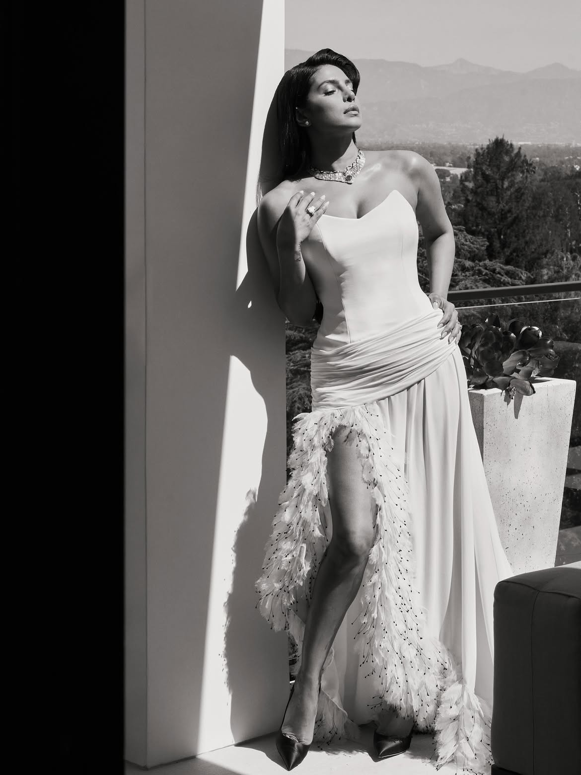 Black and white portrait of Priyanka Chopra in a strapless gown with a dramatic feathered thigh-high slit