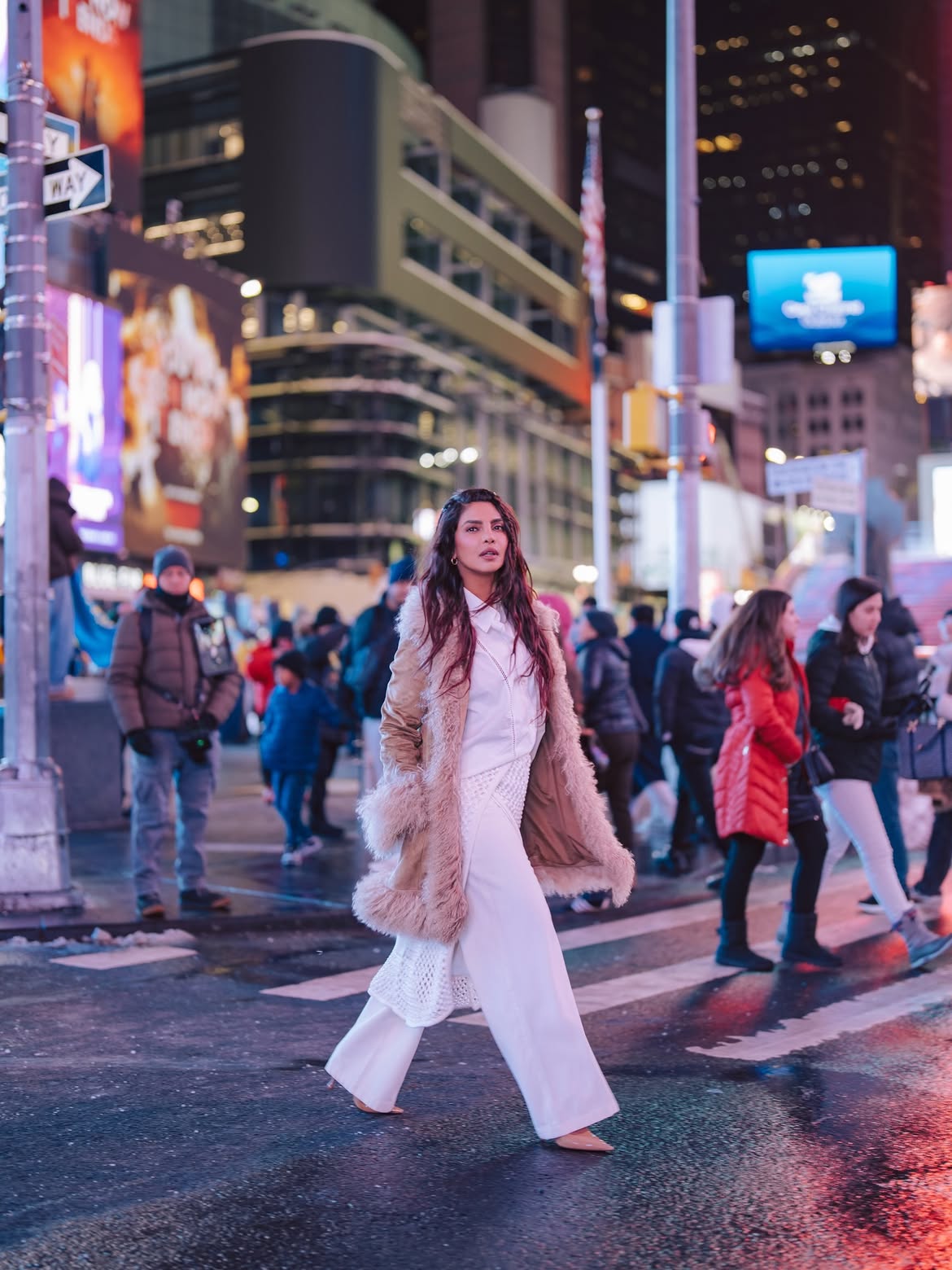 Priyanka Chopra crossing a New York City street at night in an all-white outfit layered with a shearling coat