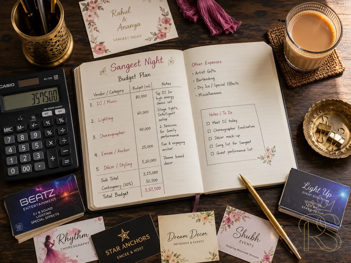 Indian wedding budget planning flat-lay for sangeet night — an open notebook with hand-written vendor categories and budget allocations (DJ, Lighting, Choreographer, Emcee, Décor), a calculator, a brass pen holder, scattered vendor visiting cards, a glass of chai, warm natural light from the side, editorial flat-lay photography, top-down, dark wood surface, no smartphone visible, planning and budgeting aesthetic