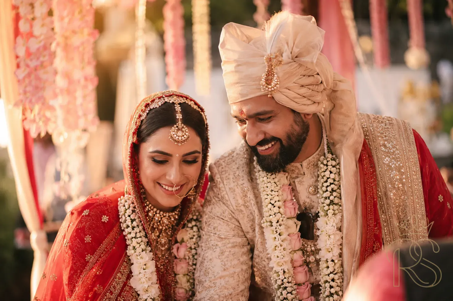 Indian bride and groom under a flower-draped mandap at golden hour